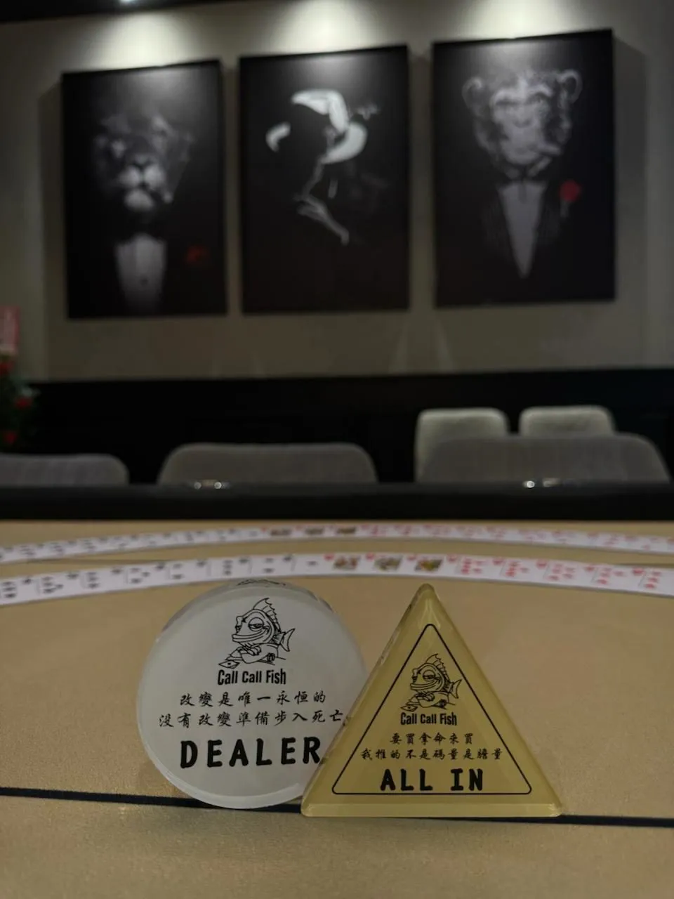 叩叩魚德州撲克競技協會牌桌上的白色圓形 DEALER 牌與金色三角形 ALL IN 牌，都印著協會的魚標誌與一句中文標語