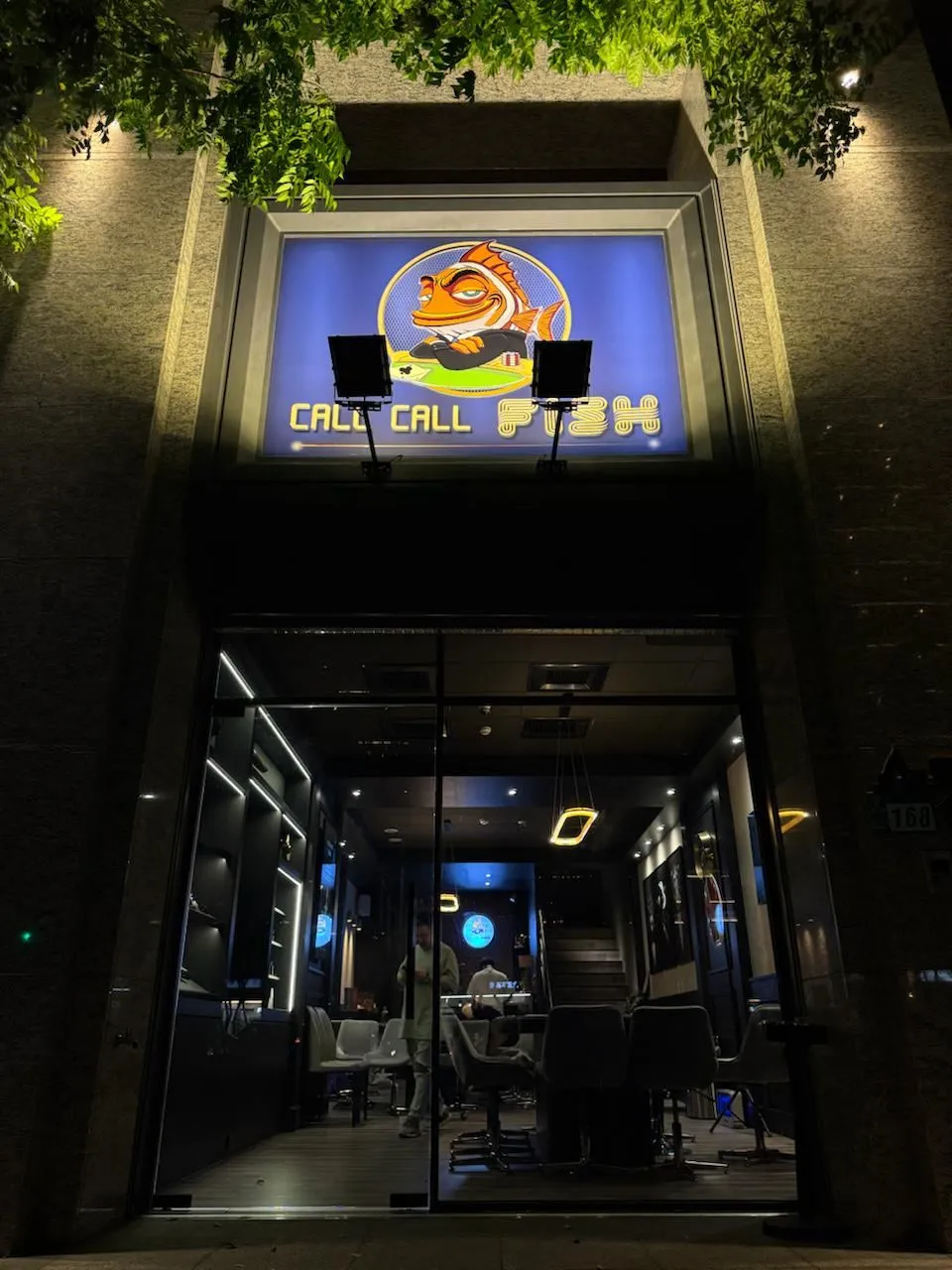 叩叩魚德州撲克競技協會入夜後的店門口，發光招牌上是一條戴墨鏡、雙手抱胸的橘色魚，旁邊寫著 CALL CALL FISH